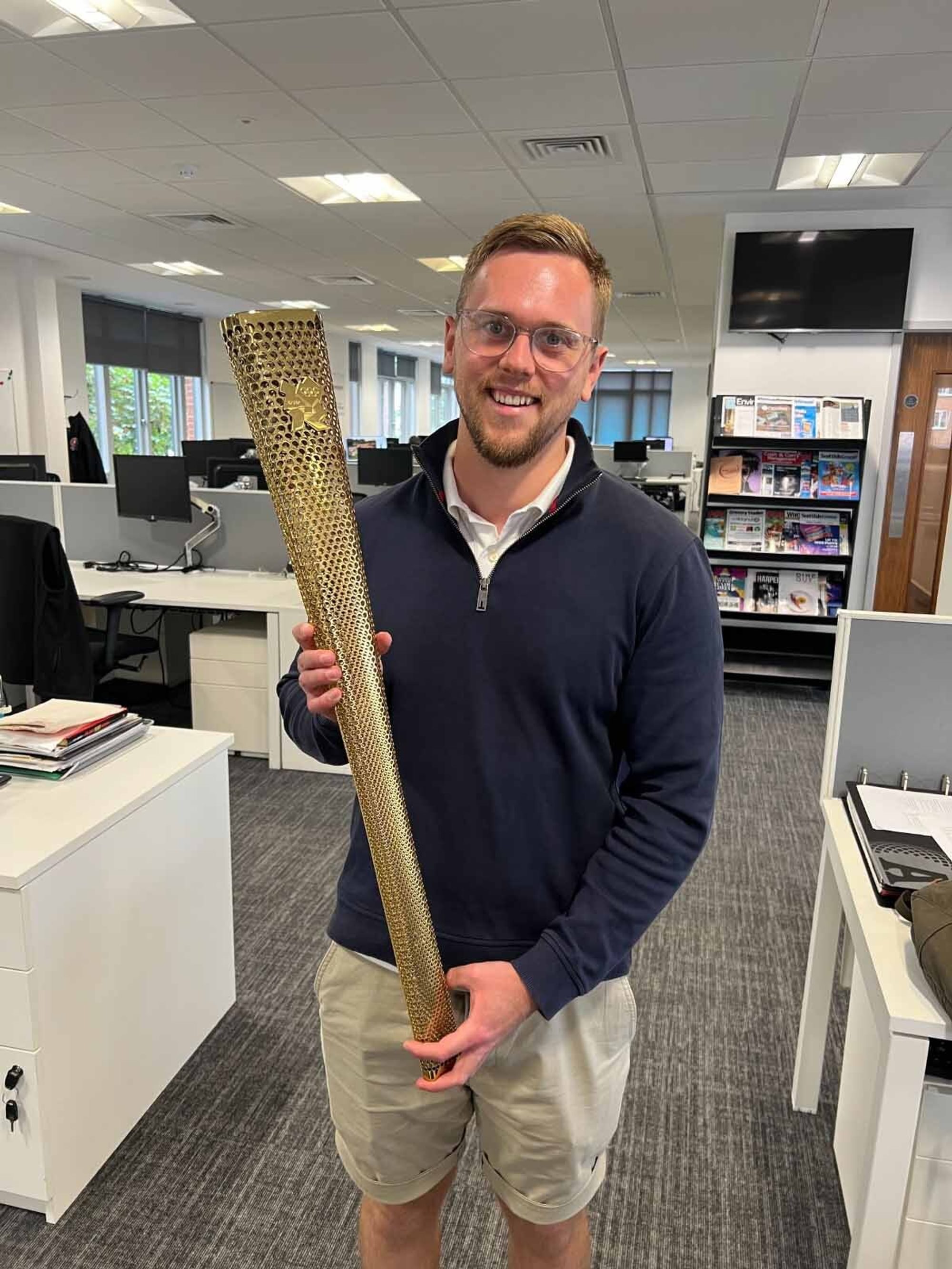 A man poses in an office with an official olympic torch from the 2012 games