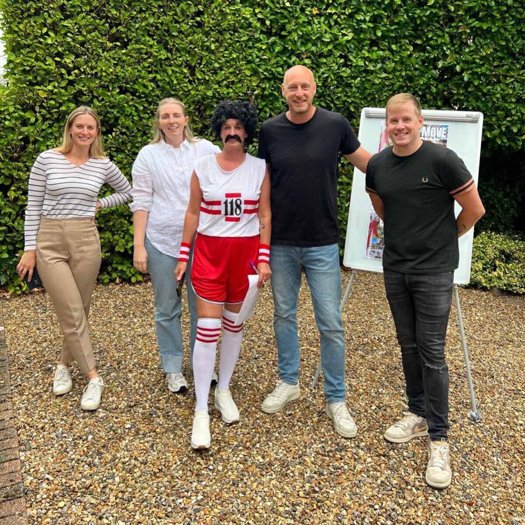 A mix of people together outdoors with someone dressed in retro sports clothes ready to take part