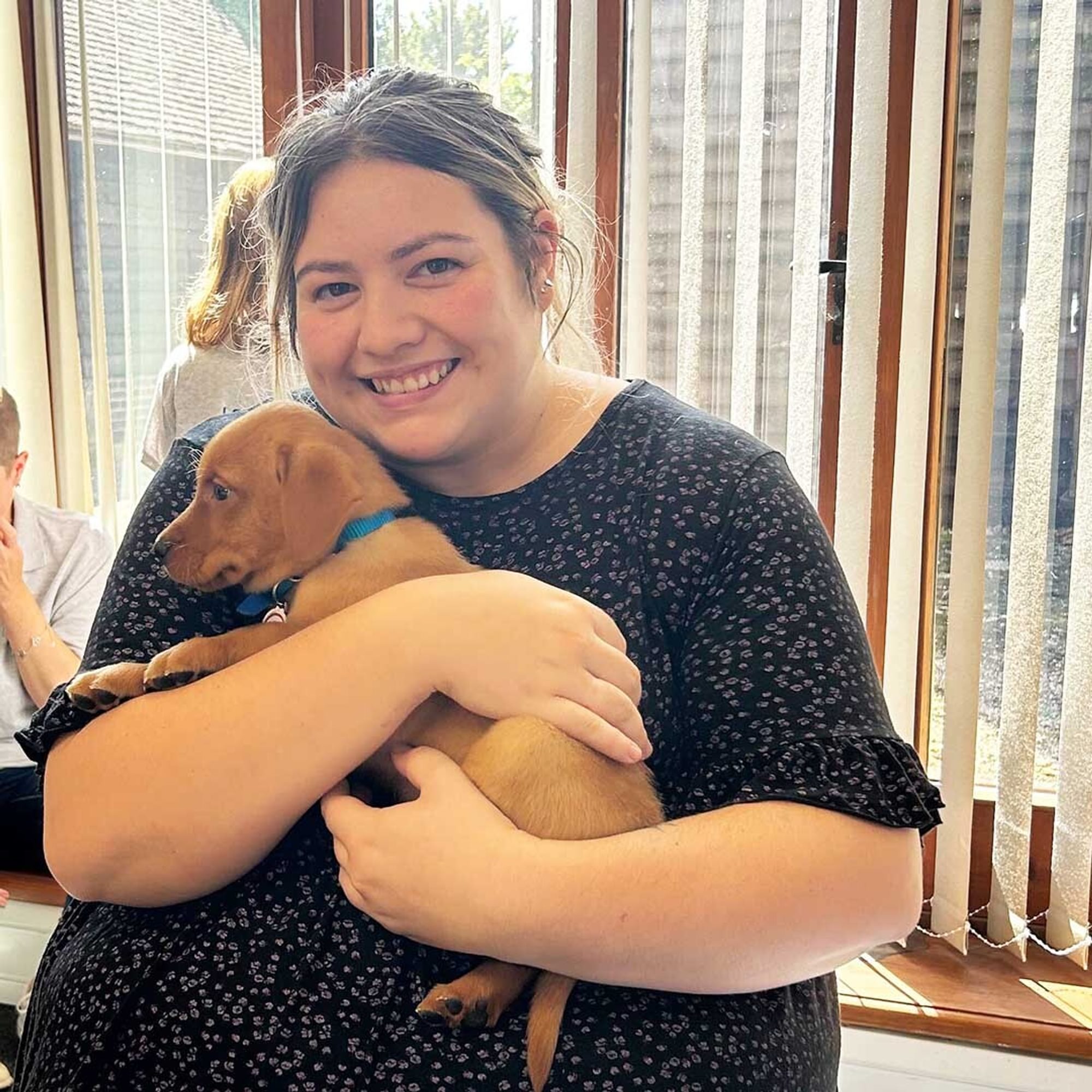 A smiling woman gives a Hypo Hounds puppy a close cuddle