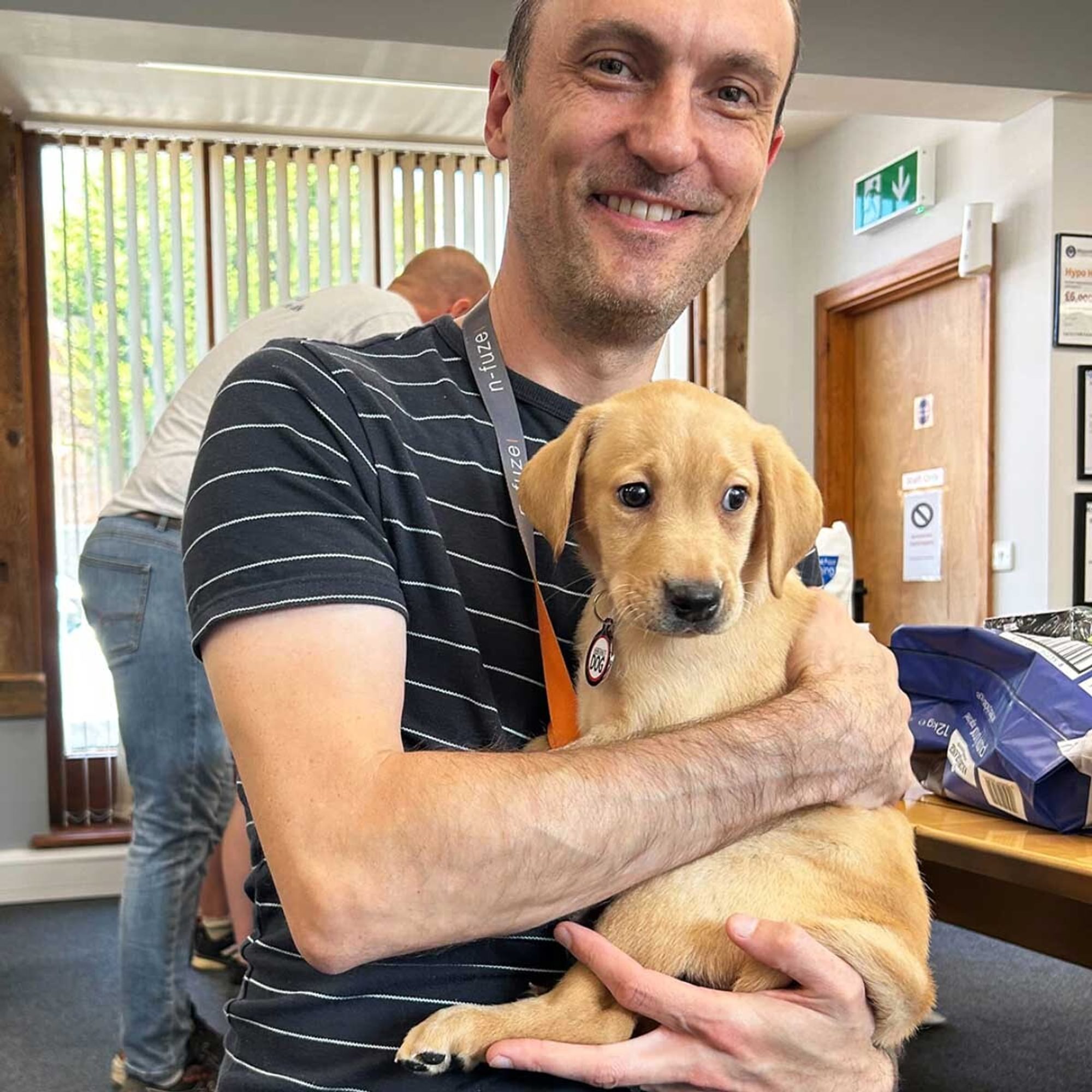 A smiling man holds a Hypo Hounds puppy to his chest