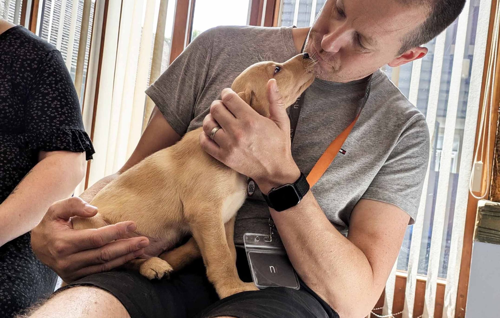 A small tan coloured puppy sits on a man’s lap and sniffs at his face