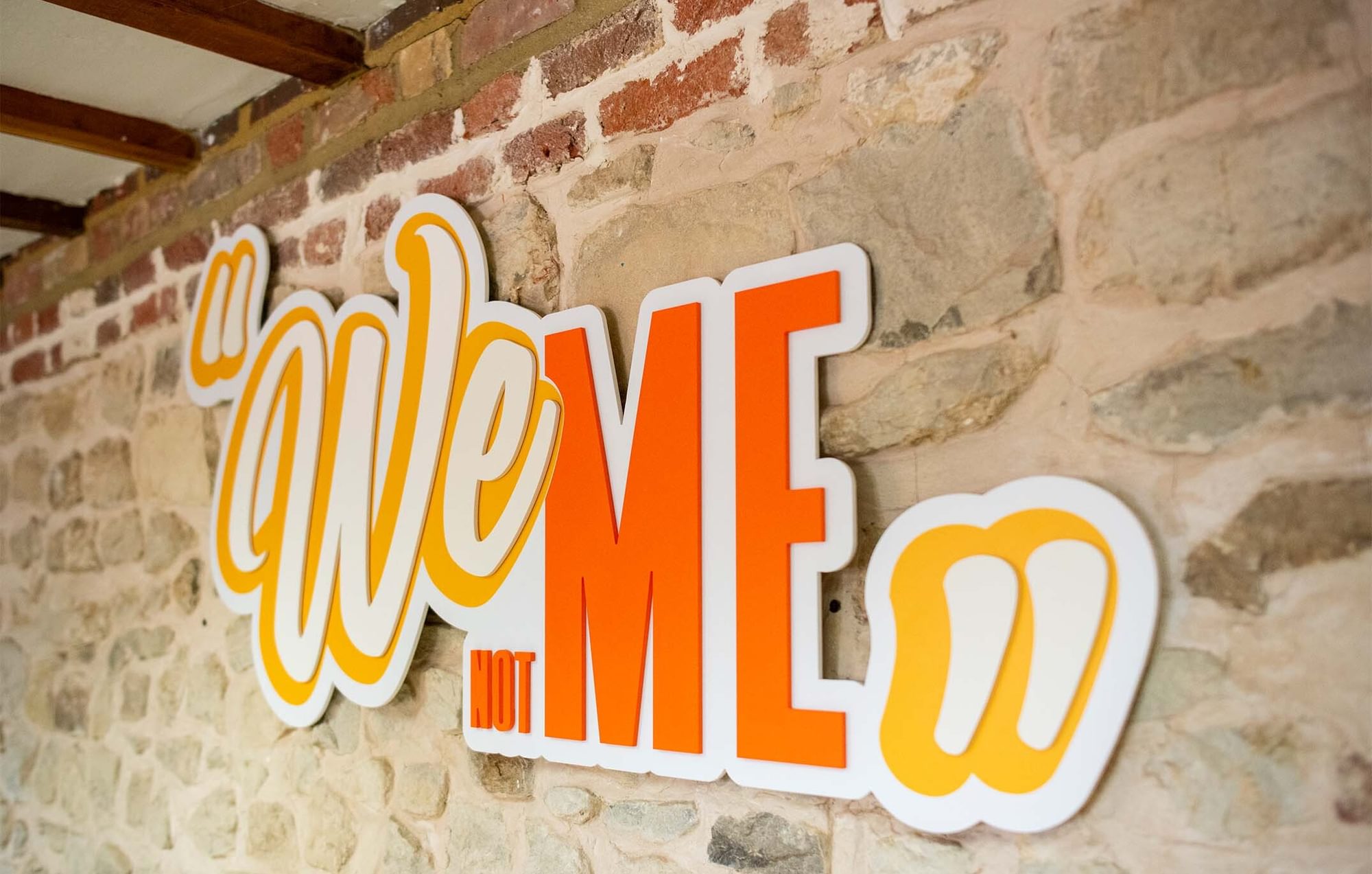 A sign on a stone wall says “We not me”