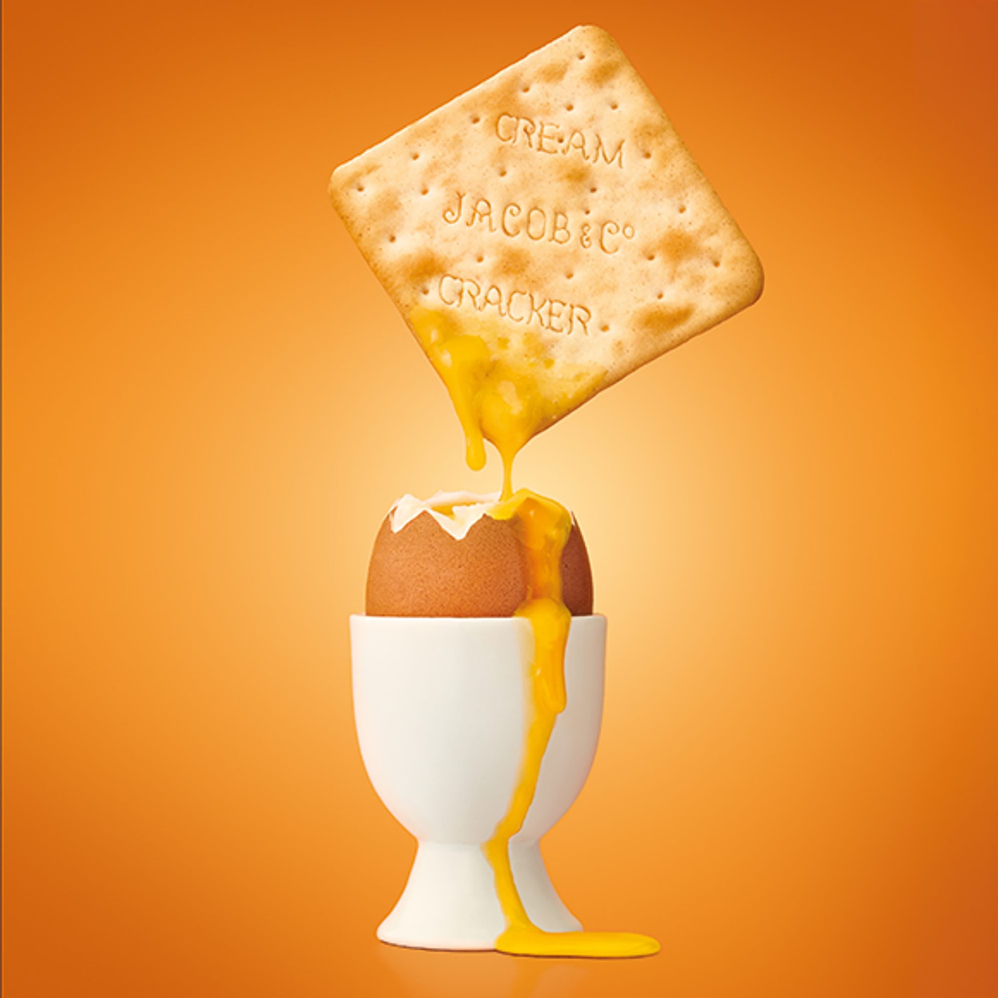 A Jacobs cream cracker dipping into a boiled egg with yolk running down the egg cup