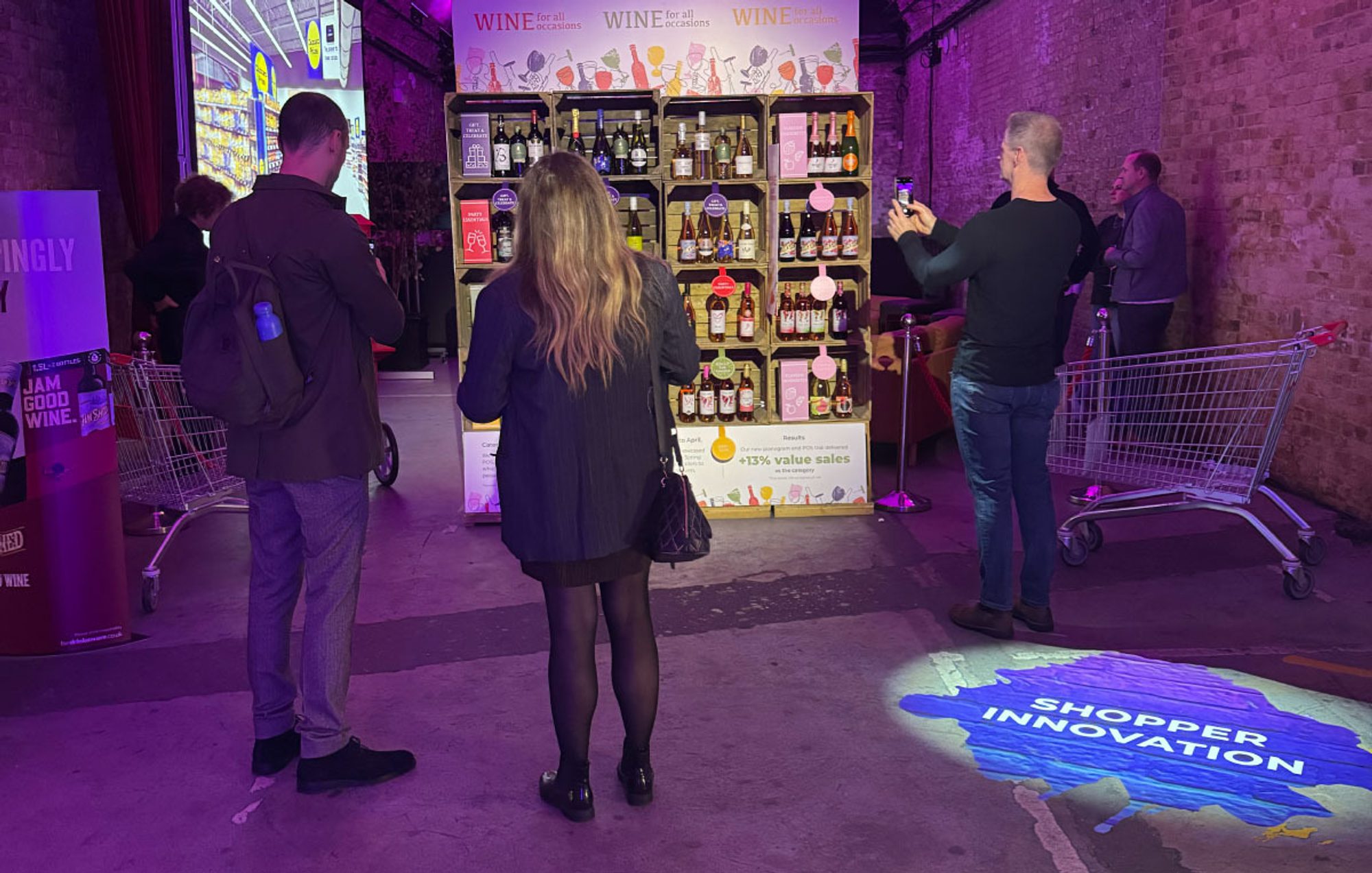 3 of the n-fuze team at the House of Accolade (now Vinarchy) 2024 event with branded shelving, digital wall display and shopping trolleys.